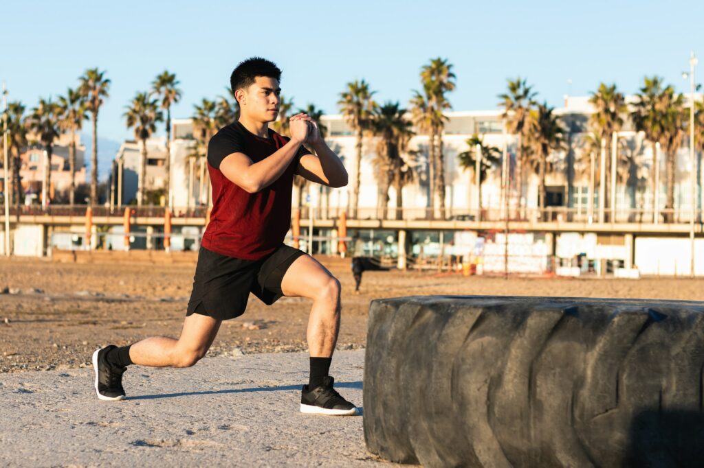 Ethnic sporty man doing lunges near tire