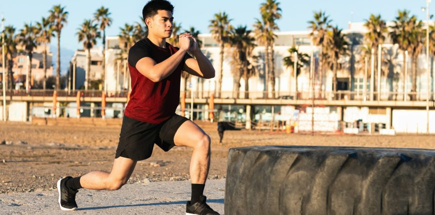 Ethnic sporty man doing lunges near tire